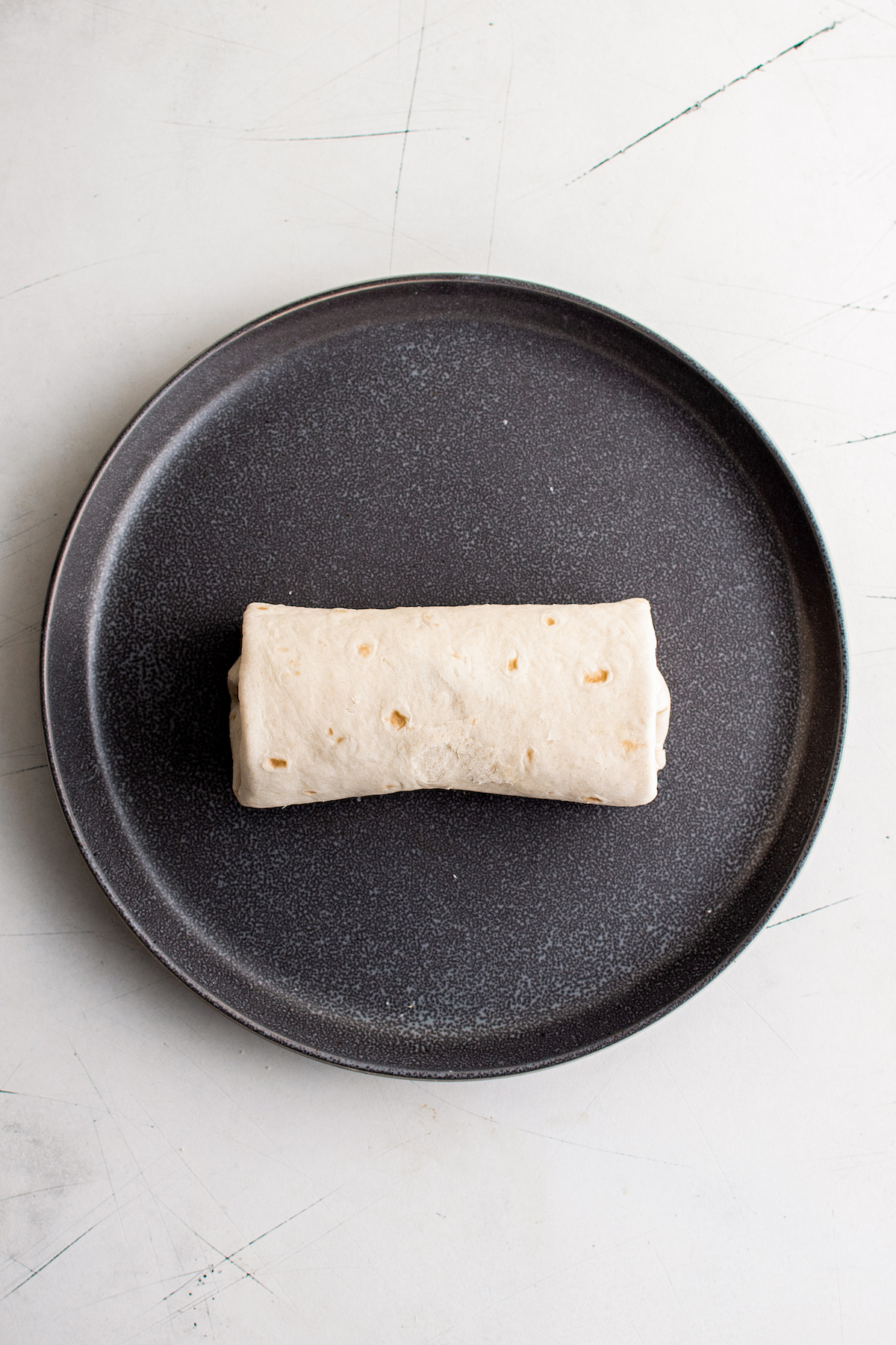 A rolled-up burrito on a black plate.