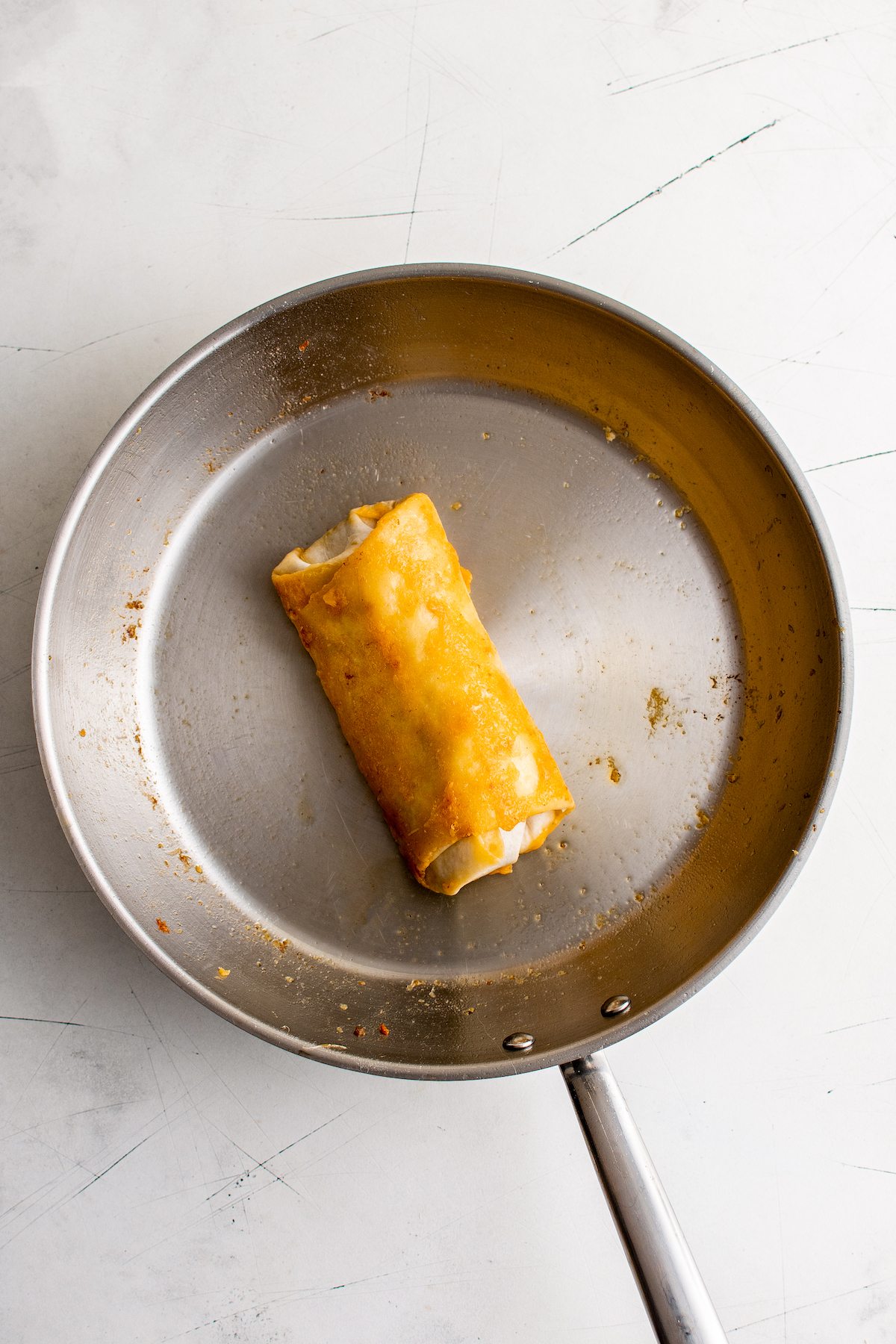 A burrito rolled up in melted cheese in a skillet.