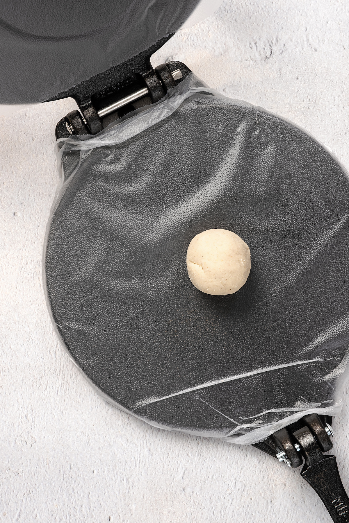 Placing a ball of dough on top of plastic wrap in a tortilla press.