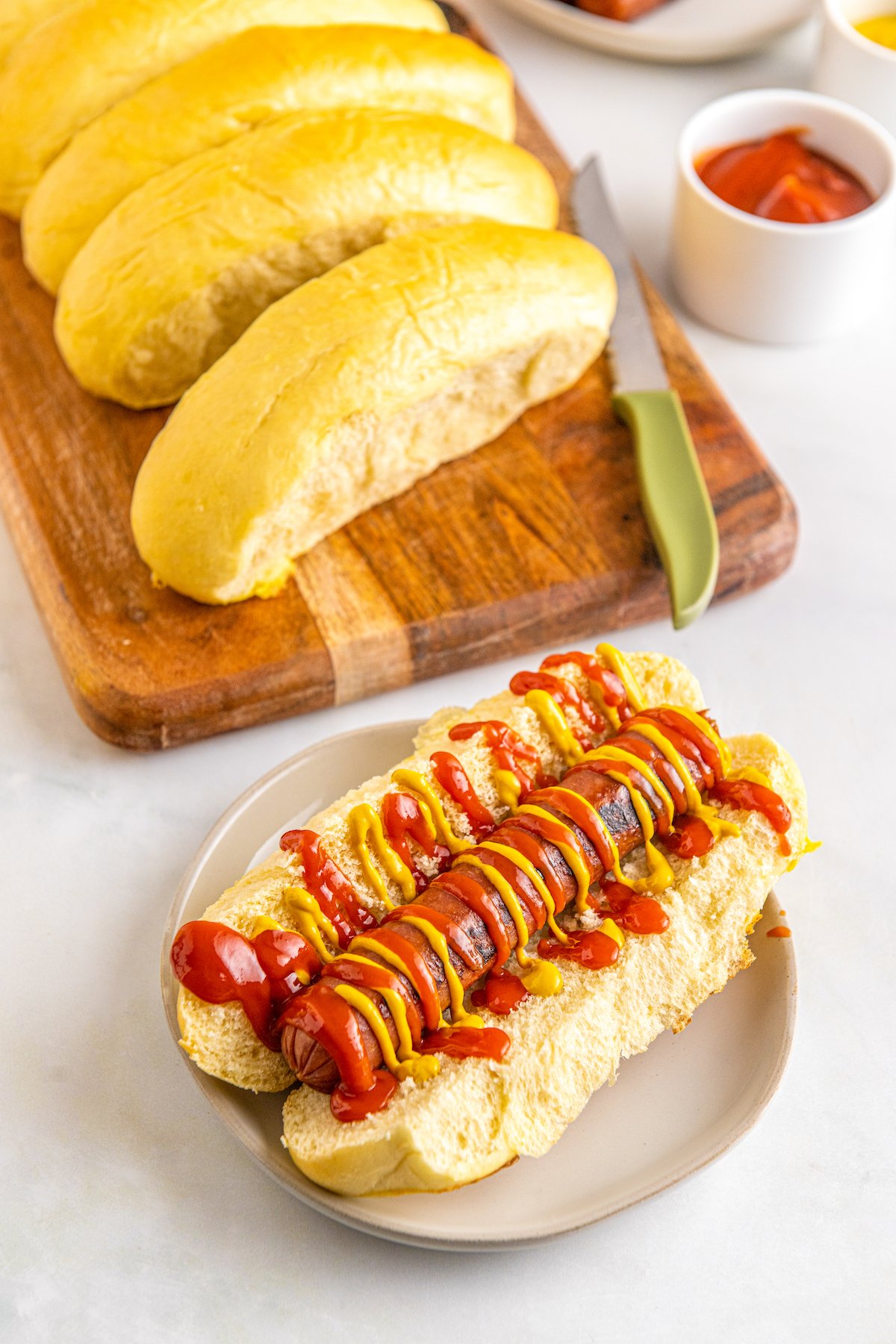 Homemade hot dog buns with one spit open and topped with a frankfurter, ketchup, and mustard.