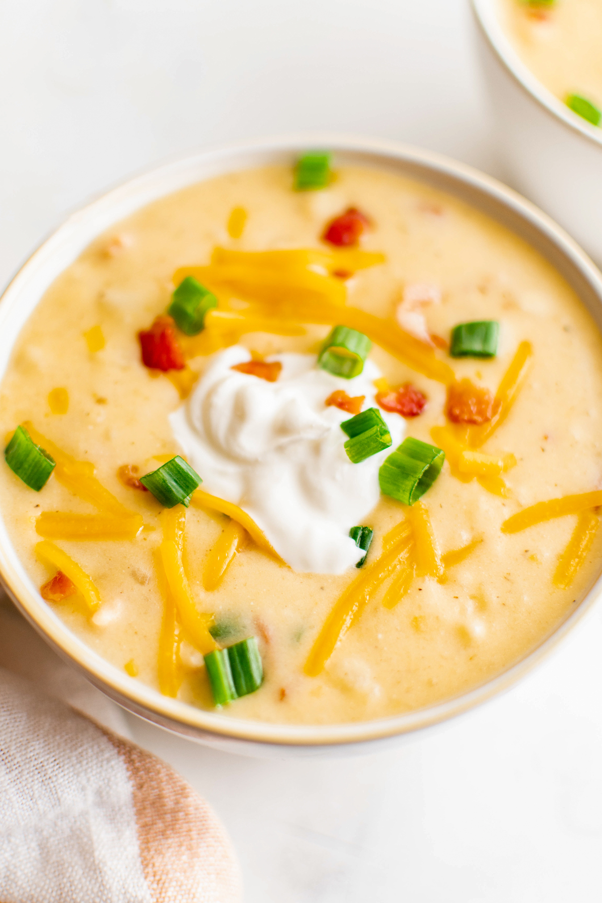 A bowl of potato soup garnished with sour cream, cheddar cheese, green onion, and bacon bits.