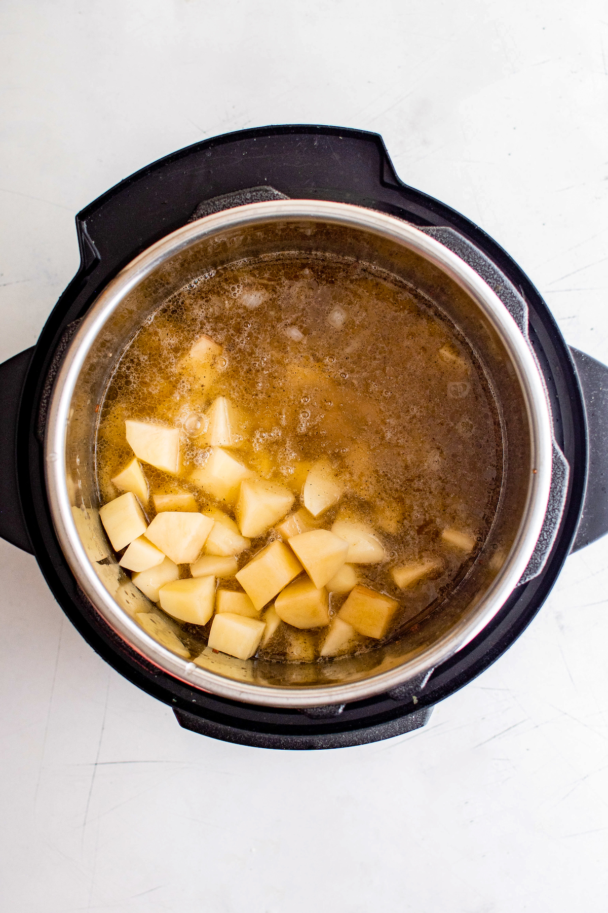 Potatoes, broth, and other soup ingredients in an electric pressure cooker.