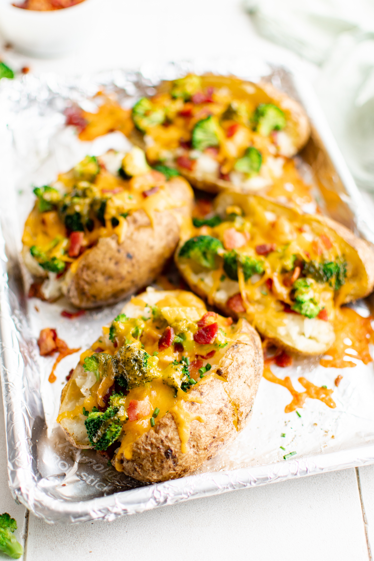 A foil lined sheet of baked potatoes with toppings.