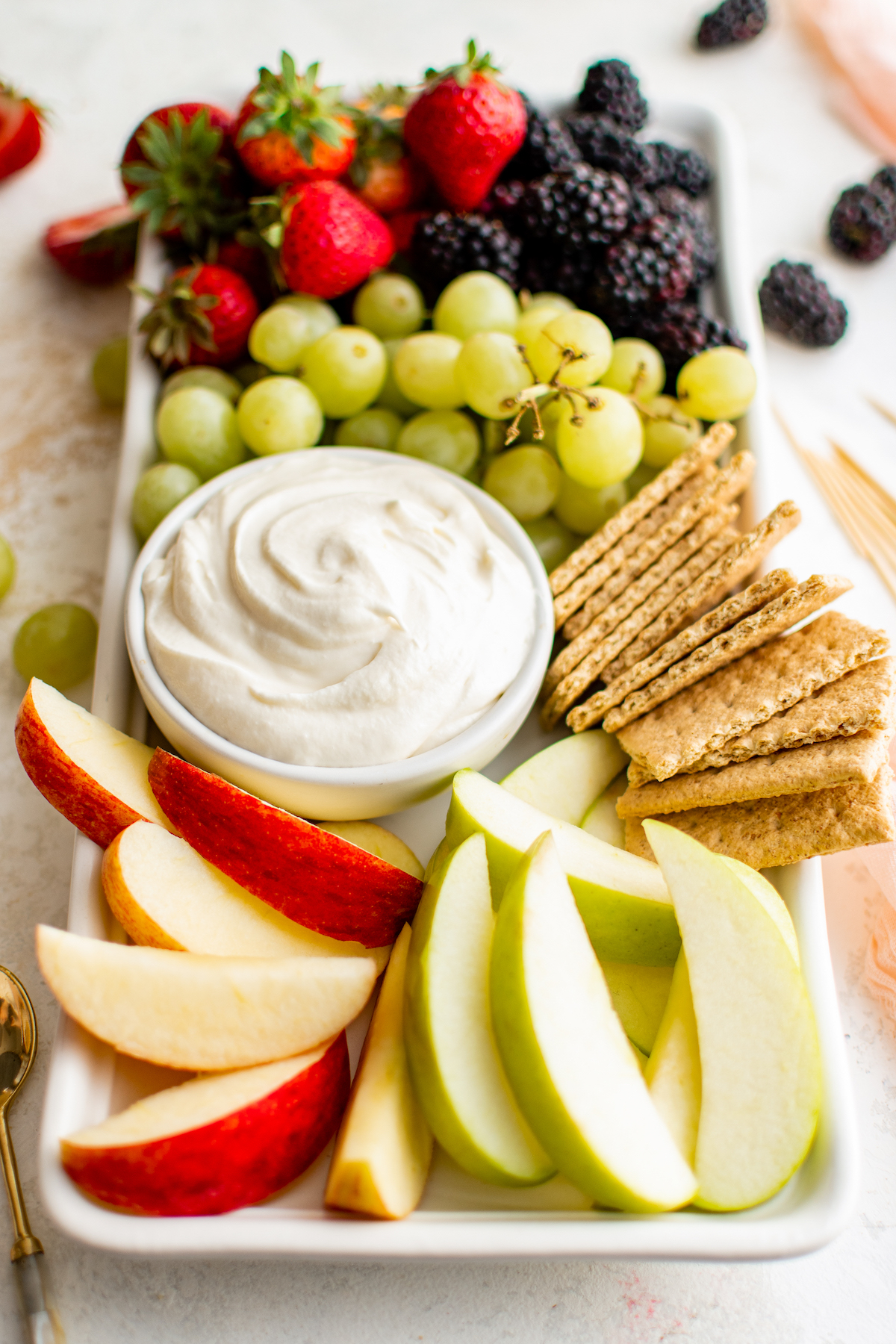 Grapes, apples, crackers, berries, and creamy sauce on a tray.