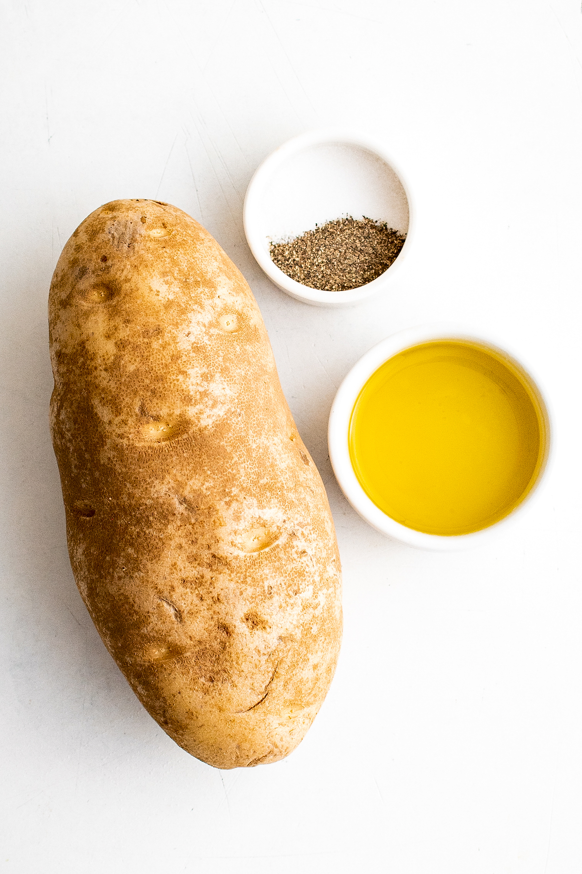 A russet potato, a dish of salt and pepper, and a dish of oil.