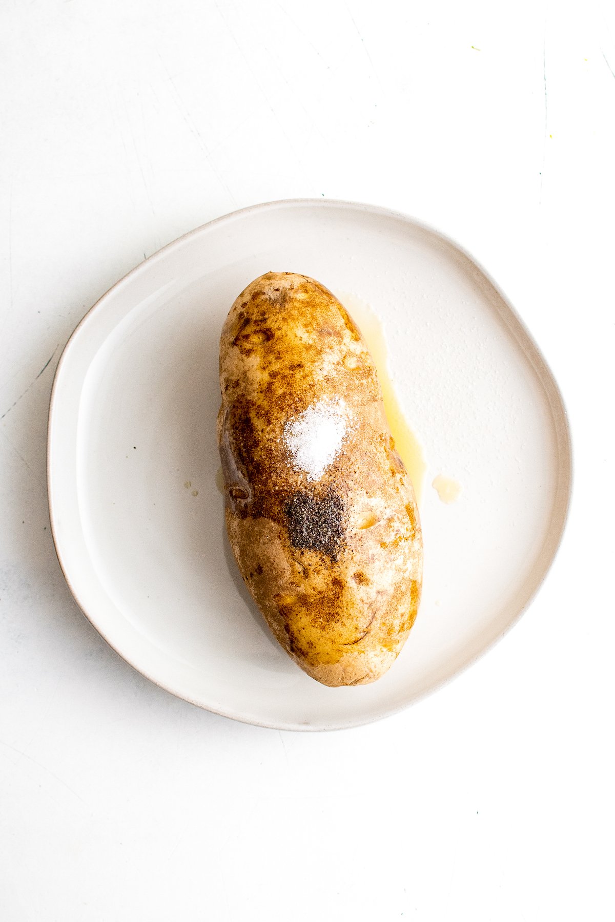 A potato topped with oil, salt, and pepper.