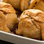 Close-up shot of two dumplings in a baking dish with cinnamon sauce and pastry leaves.