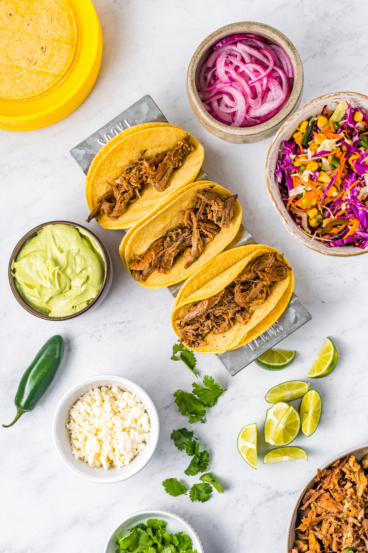 Three tacos with pork in them, and other ingredients arranged around the tacos in small dishes.