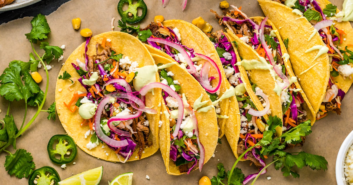 Pulled pork tacos lined up on a parchment-paper board.