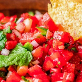 A bowl of strawberry watermelon salsa being scooped up with a tortilla chip.