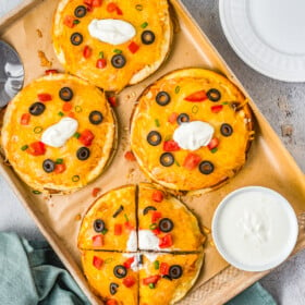 Four Taco Bell Mexican Pizza copycats on a baking sheet with a bowl of sour cream.