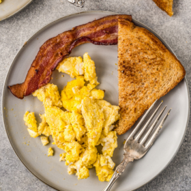 Scrambled eggs on a plate with toast and bacon.