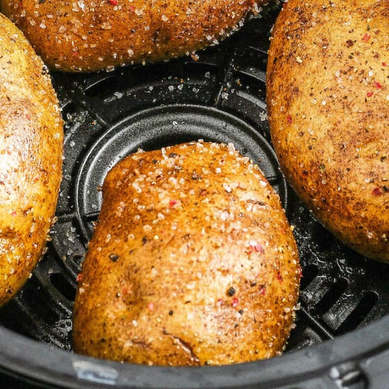 Four potatoes in an air fryer basket coated in oil, salt and pepper.