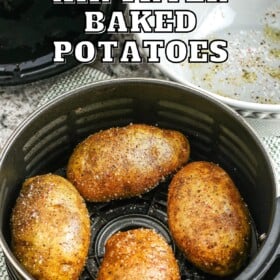 Four baked potatoes with oil and salt on them in an air fryer basket.