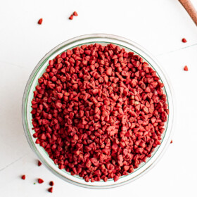 A bowl with Annatto Seeds and a few spilling out the sides.