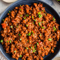 A skillet of homemade baked beans topped with chopped green onion.