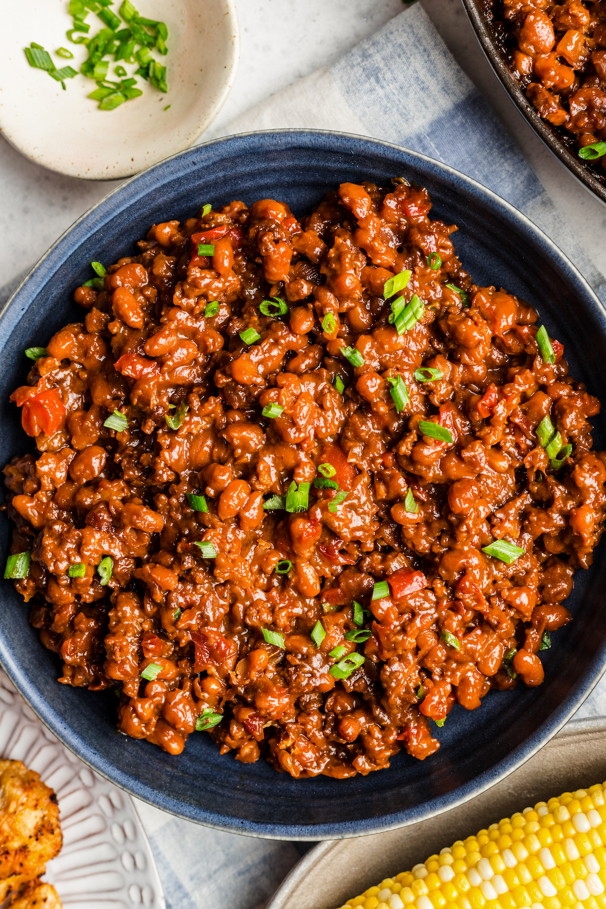 A skillet of homemade baked beans topped with chopped green onion.