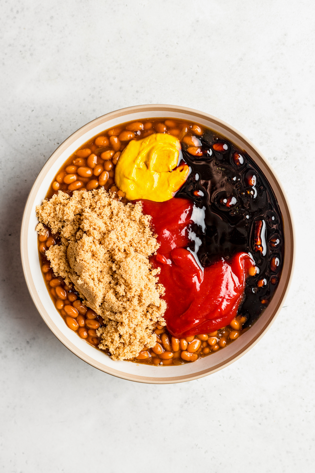 A bowl of canned baked beans with mustard, ketchup, brown sugar, and molasses dumped on top.