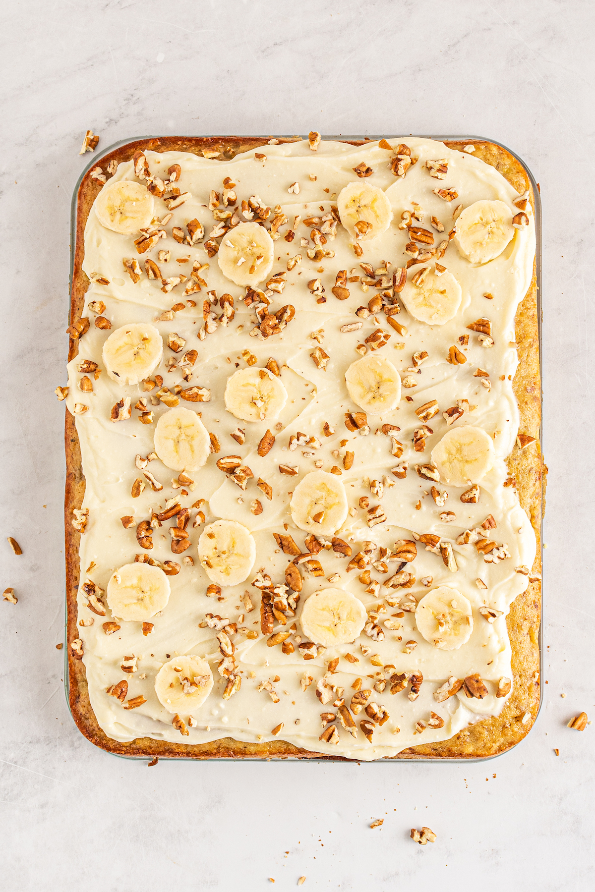 An unmolded sheet cake topped with frosting, pecans, and banana slices.