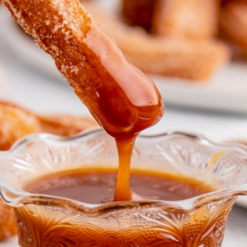 A churro being dunked into homemade salted caramel sauce.