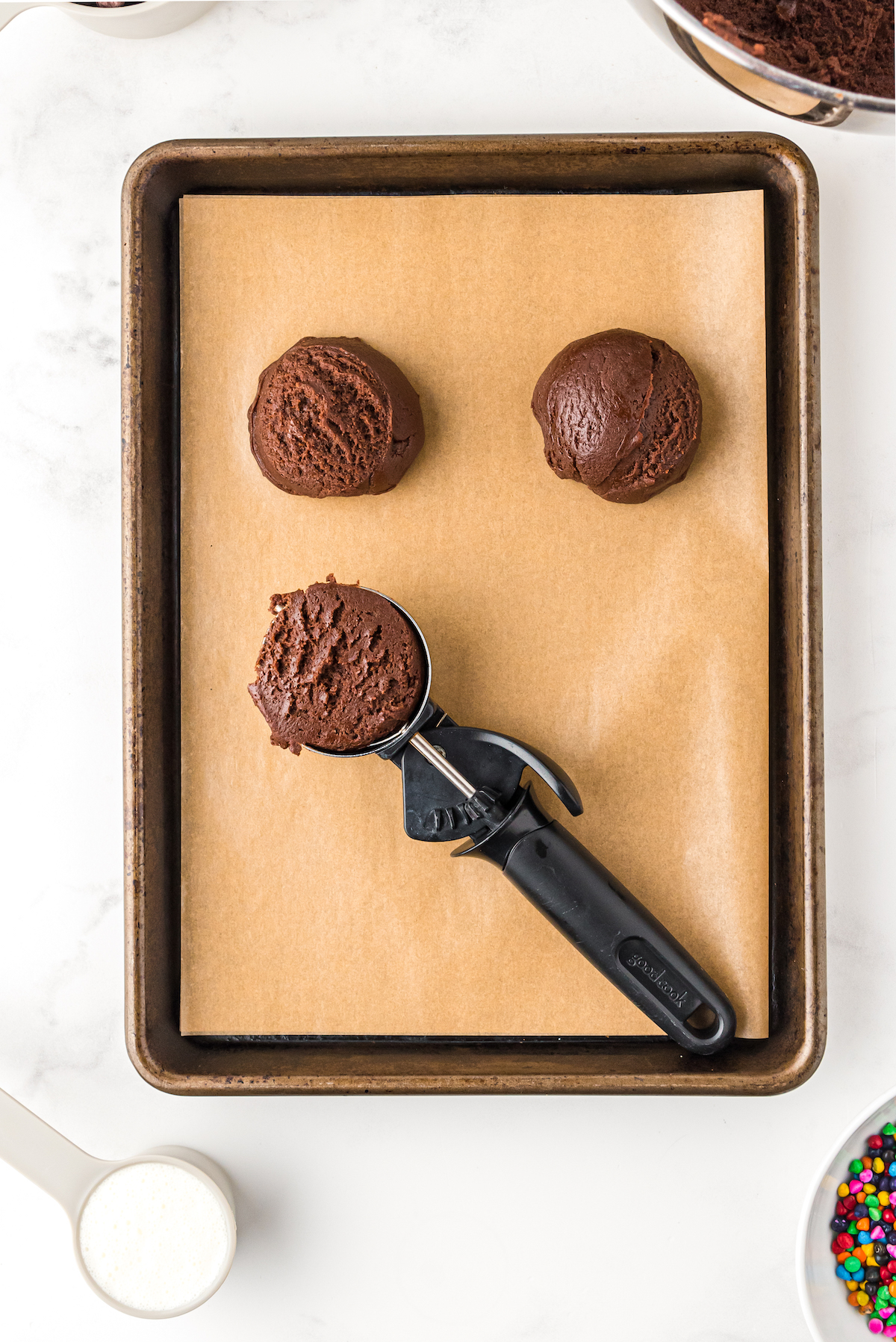 Scoops of cookie dough on a baking sheet with a cookie scoop.