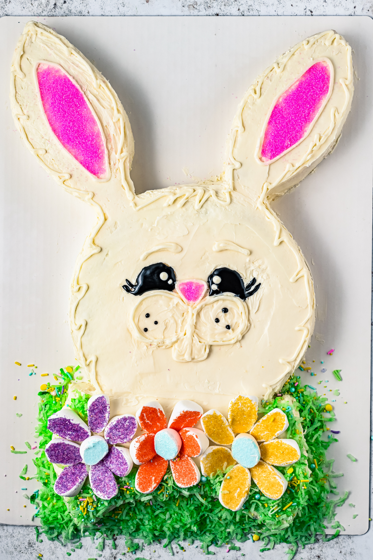 A cake shaped like a bunny, decorated with flowers and coconut grass.