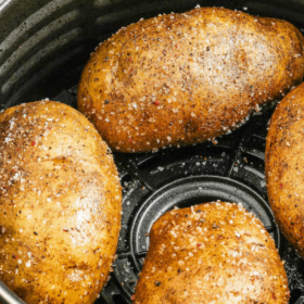 Four baked potatoes in an air fryer basket.