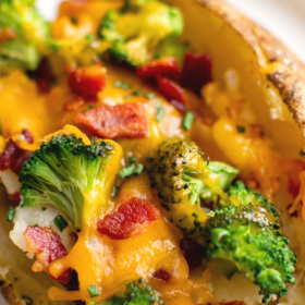 A loaded baked potato on a white plate with cheese, broccoli and bacon stuffed inside.
