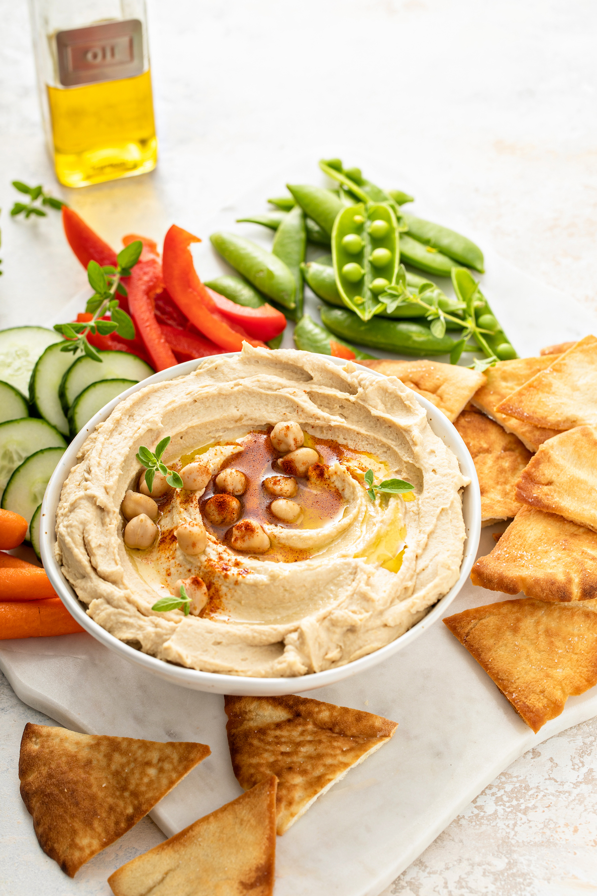 A bowl of hummus with crackers, snap peas, and other dippers.