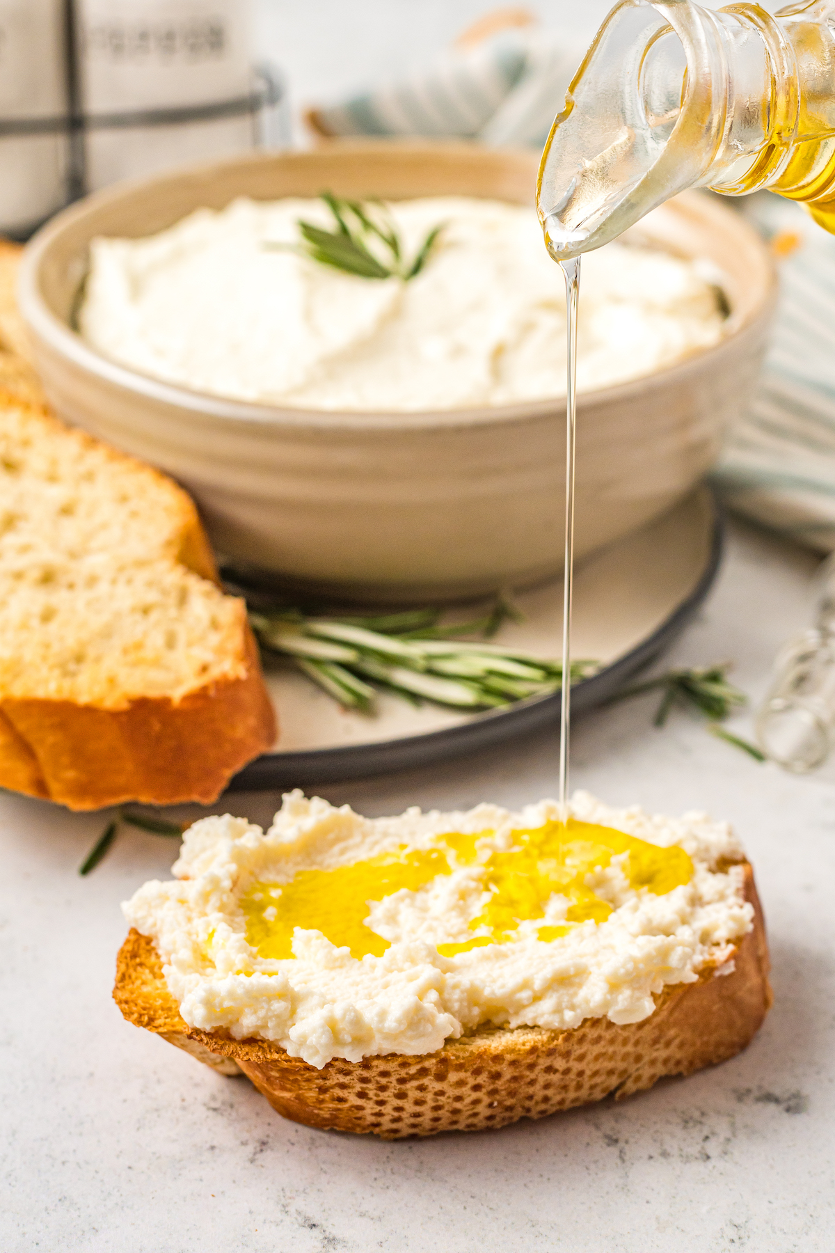 Drizzling a baguette slice  topped with ricotta with olive oil.