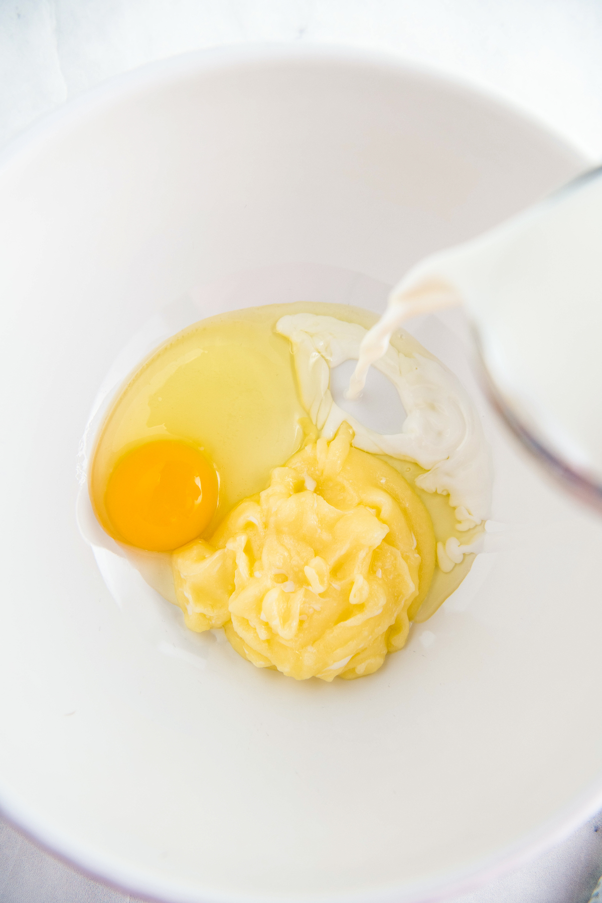 Pouring milk into a mixing bowl with eggs and butter.