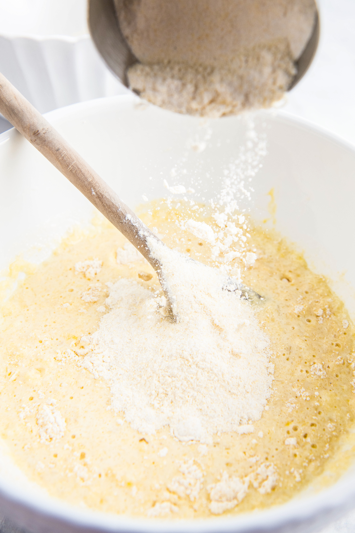 Adding dry ingredients to wet ingredients in a large white mixing bowl.