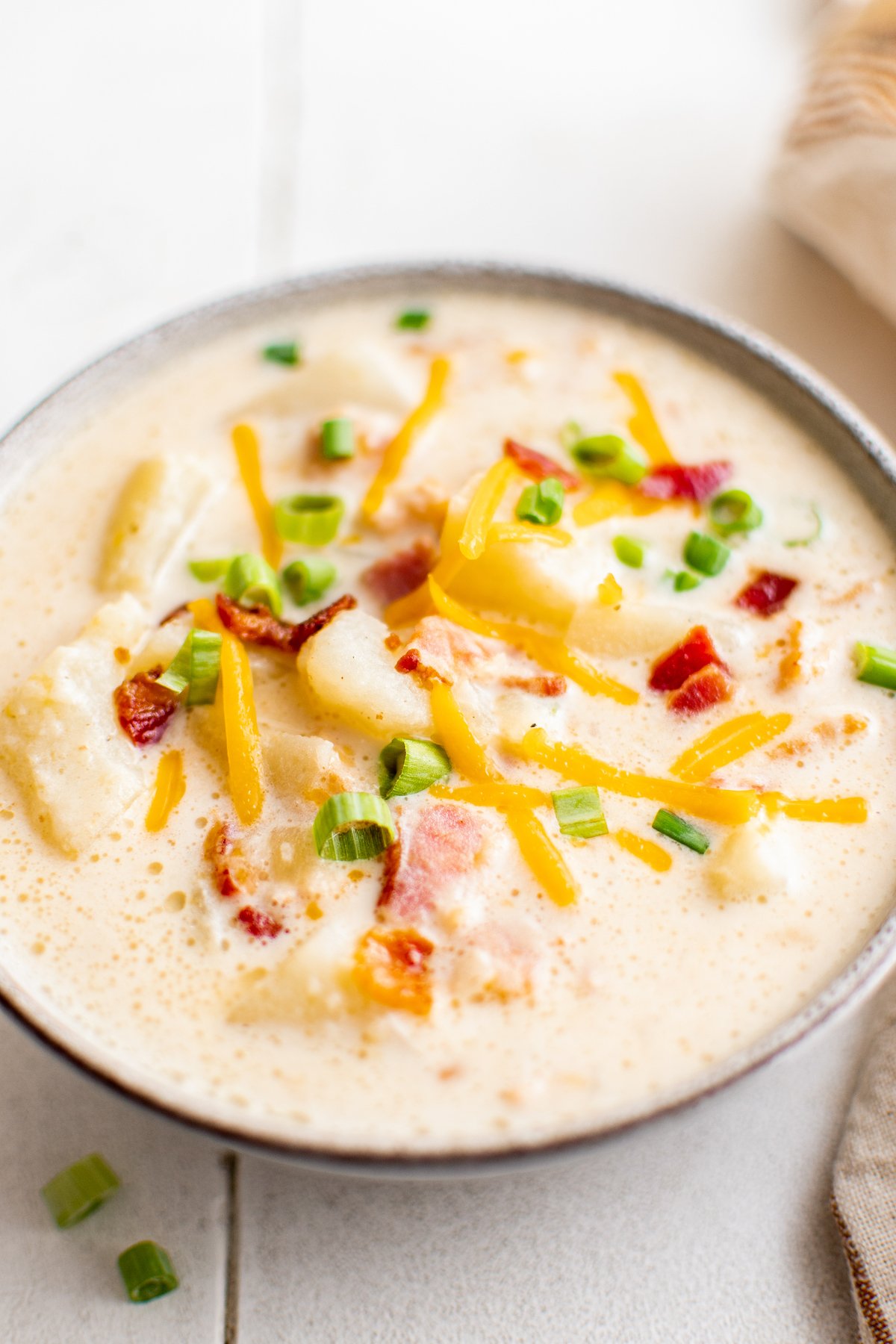 Cheddar cheese, bacon bits, and green onions sprinkled over a bowl of creamy baked potato soup.