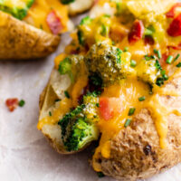 Baked potato loaded with cheese, bacon and broccoli on parchment paper.