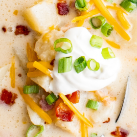 A bowl of loaded potato soup with bacon, cheese, green onion and sour cream on top.