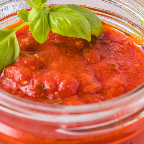 A jar of homemade marinara sauce with a sprig of basil.