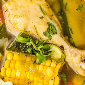 A bowl of Mexican chicken soup with corn on the cop and a chicken drumstick.
