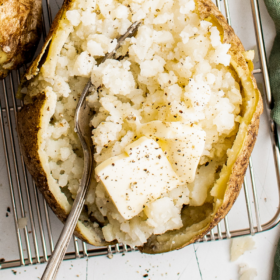 Microwave baked potato fluffed with a fork and topped with butter and seasonings.