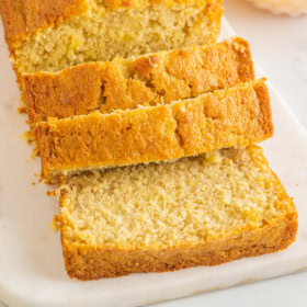 Pineapple banana bread being sliced into slices on a marble cutting board.