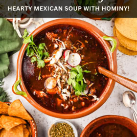 A large pot of pozole rojo with all the toppings around in bowls.