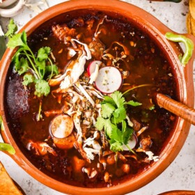 A large bowl of pozole rojo with a wooden spoon inside.