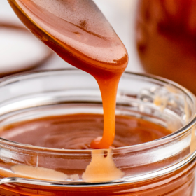A spoon drizzling caramel sauce into a jar.