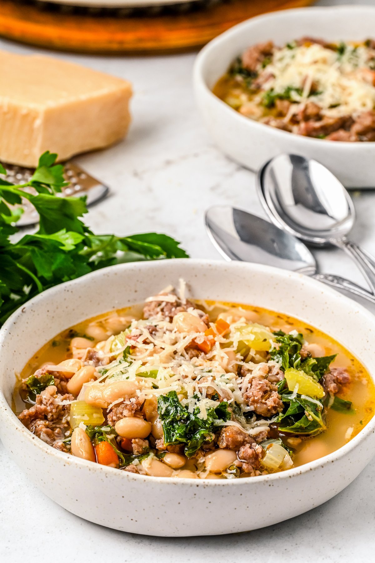 Bowls of sausage and kale soup, topped with shredded parmesan.