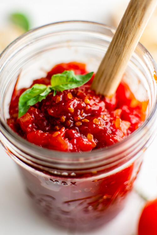 Homemade tomato jam in a jar with a wooden spoon.