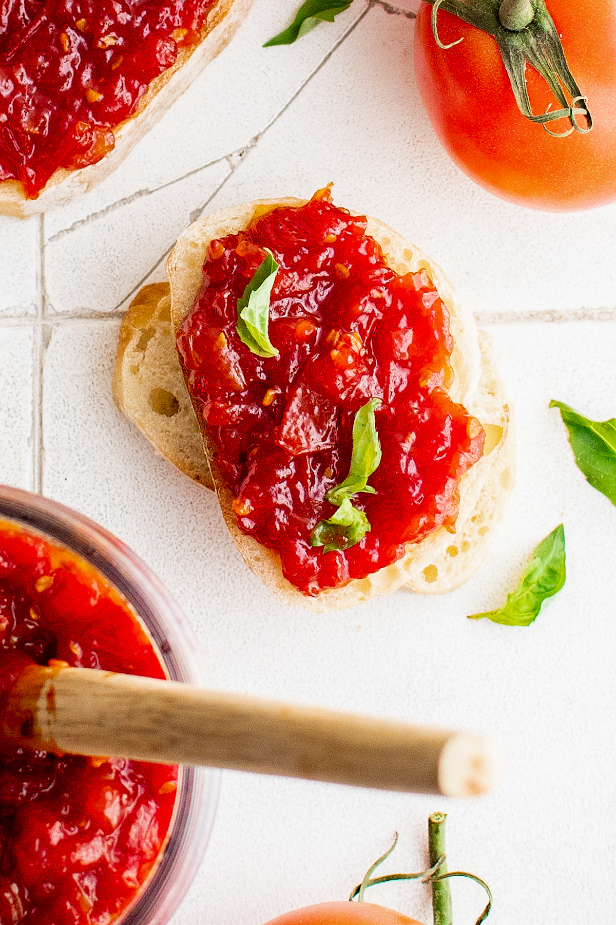 Tomato jam spread on bread, with sprigs of fresh basil leaves for garnish.