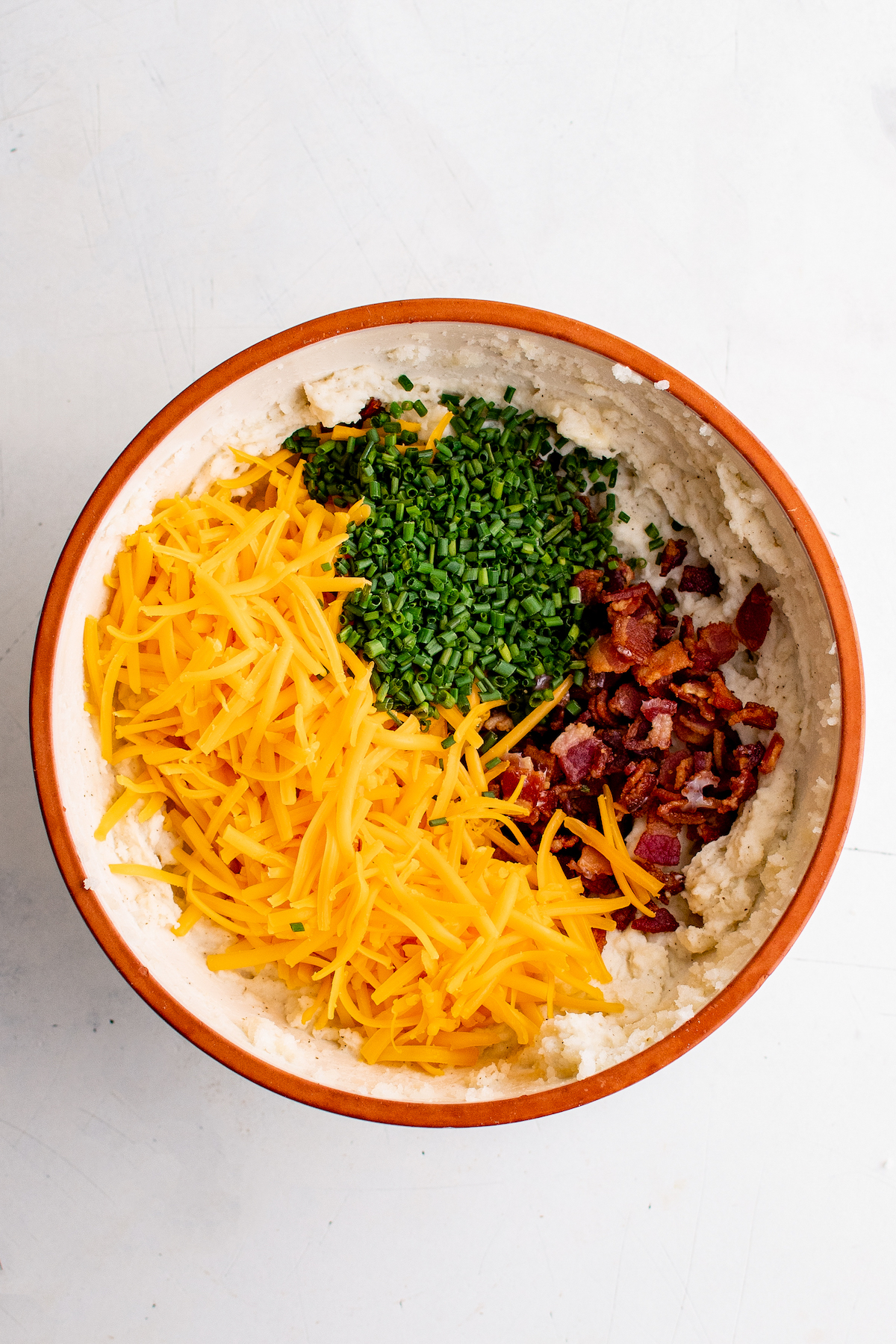 Adding shredded cheese, chives, and bacon to a mixing bowl.