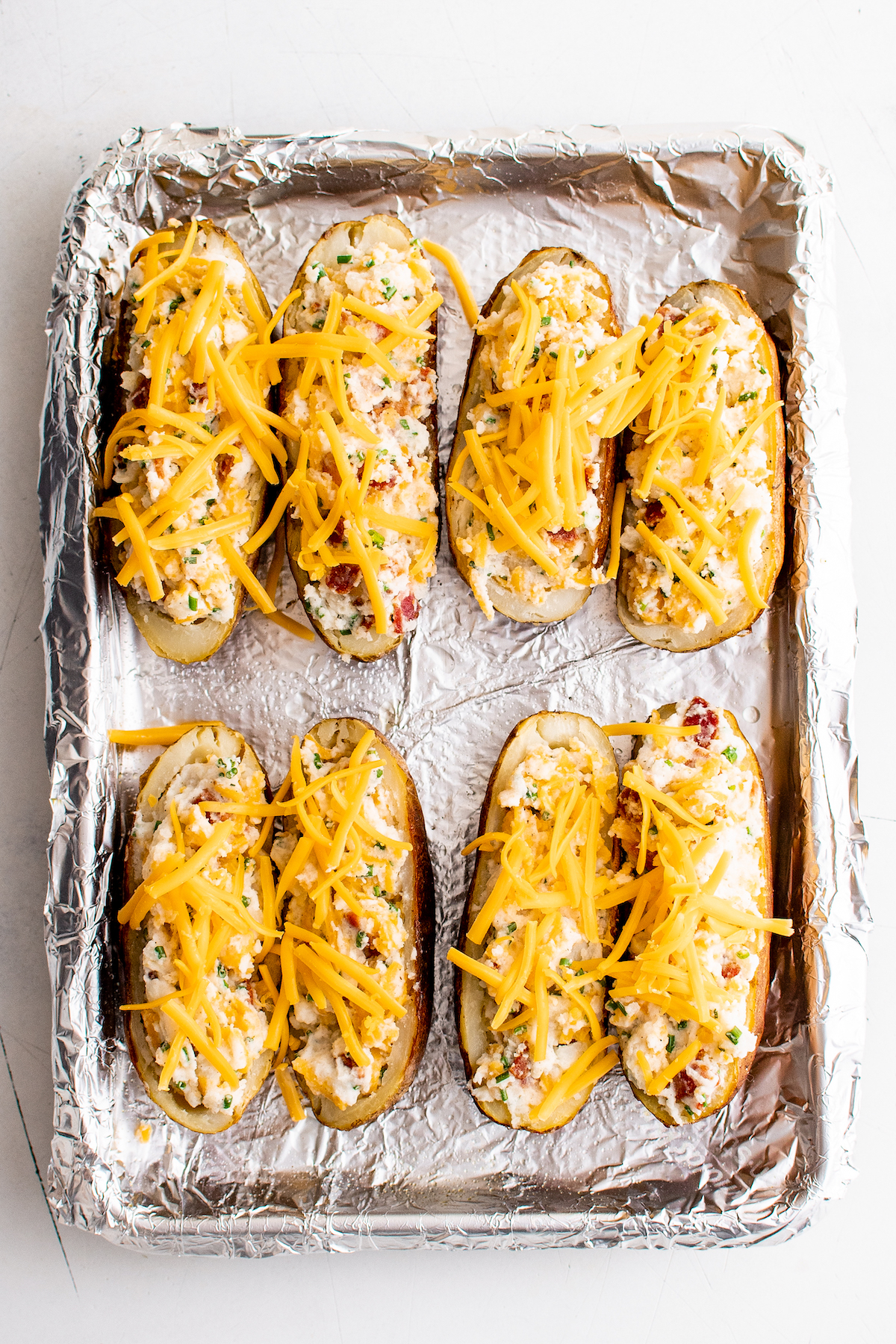 Unbaked stuffed potatoes topped with shredded cheese.
