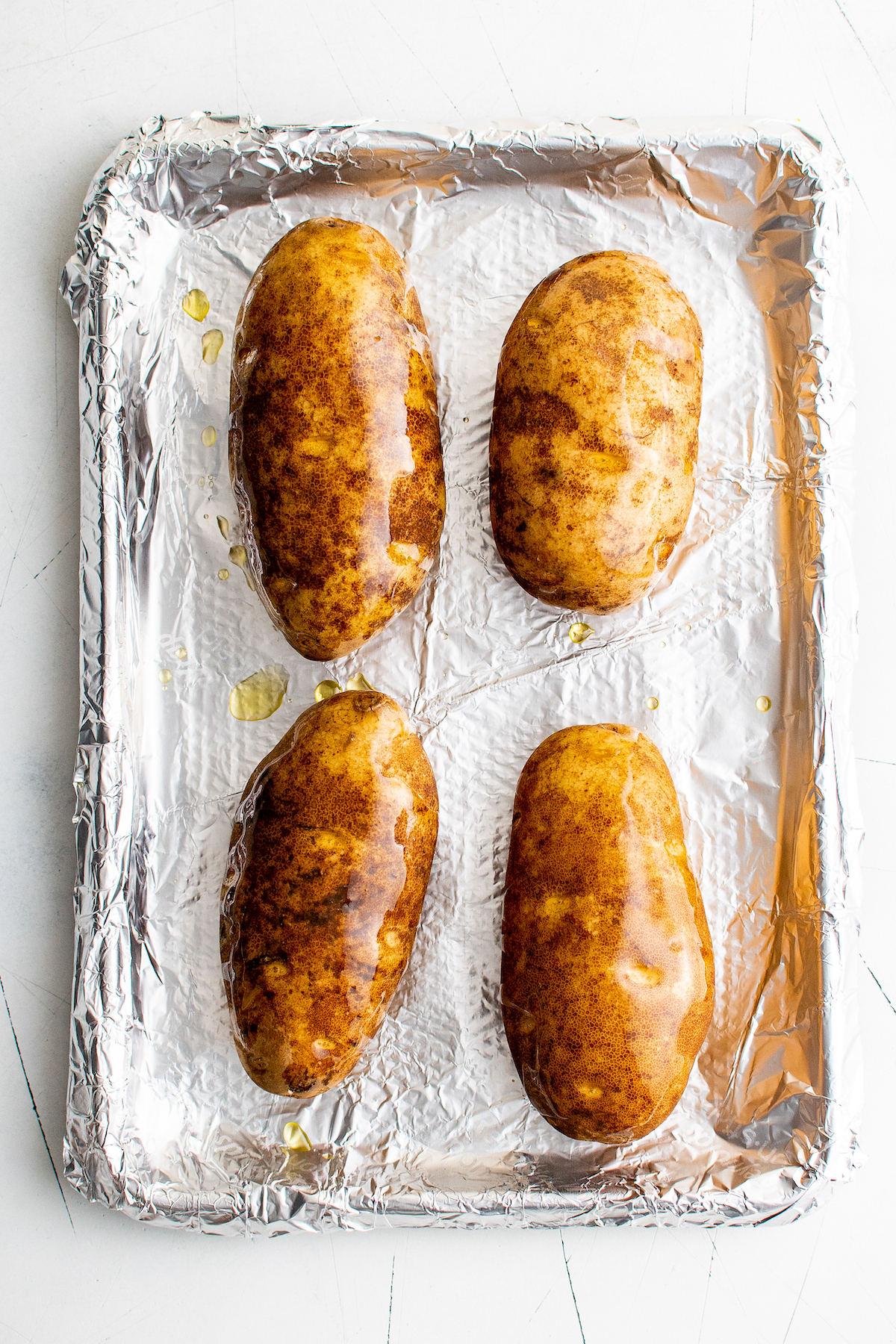 Seasoned, oiled potatoes on a foil-lined baking sheet.
