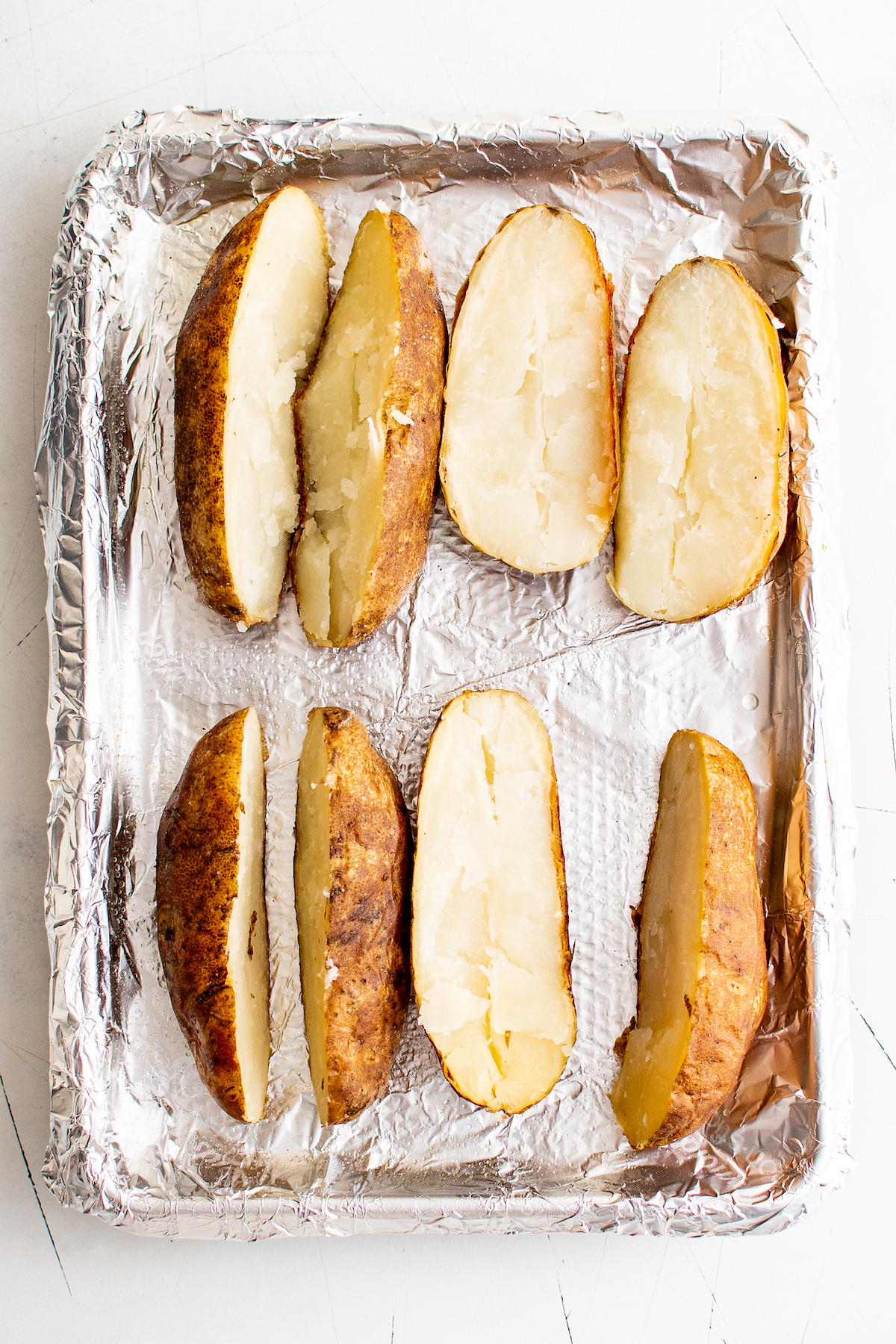 Baked potatoes sliced open on a baking sheet.