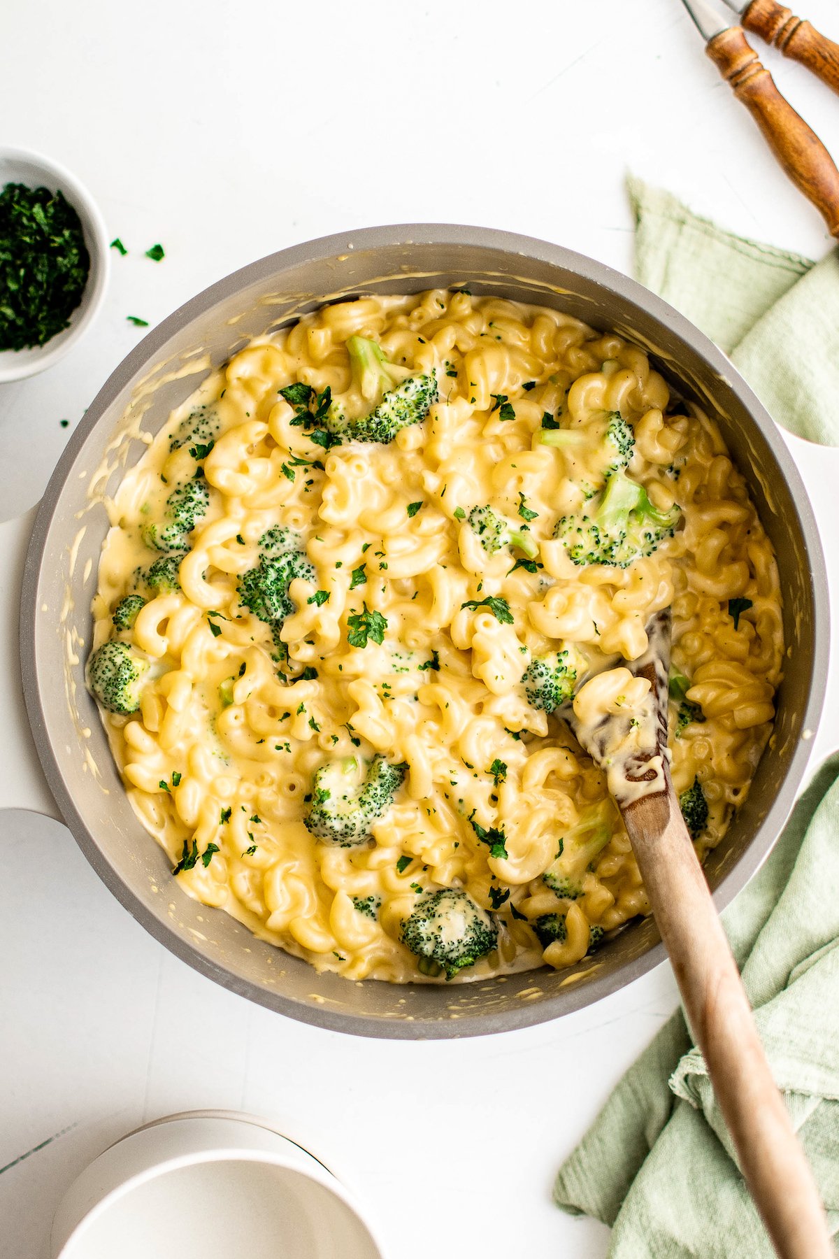 A wooden spoon resting in a pot of mac and cheese with broccoli.